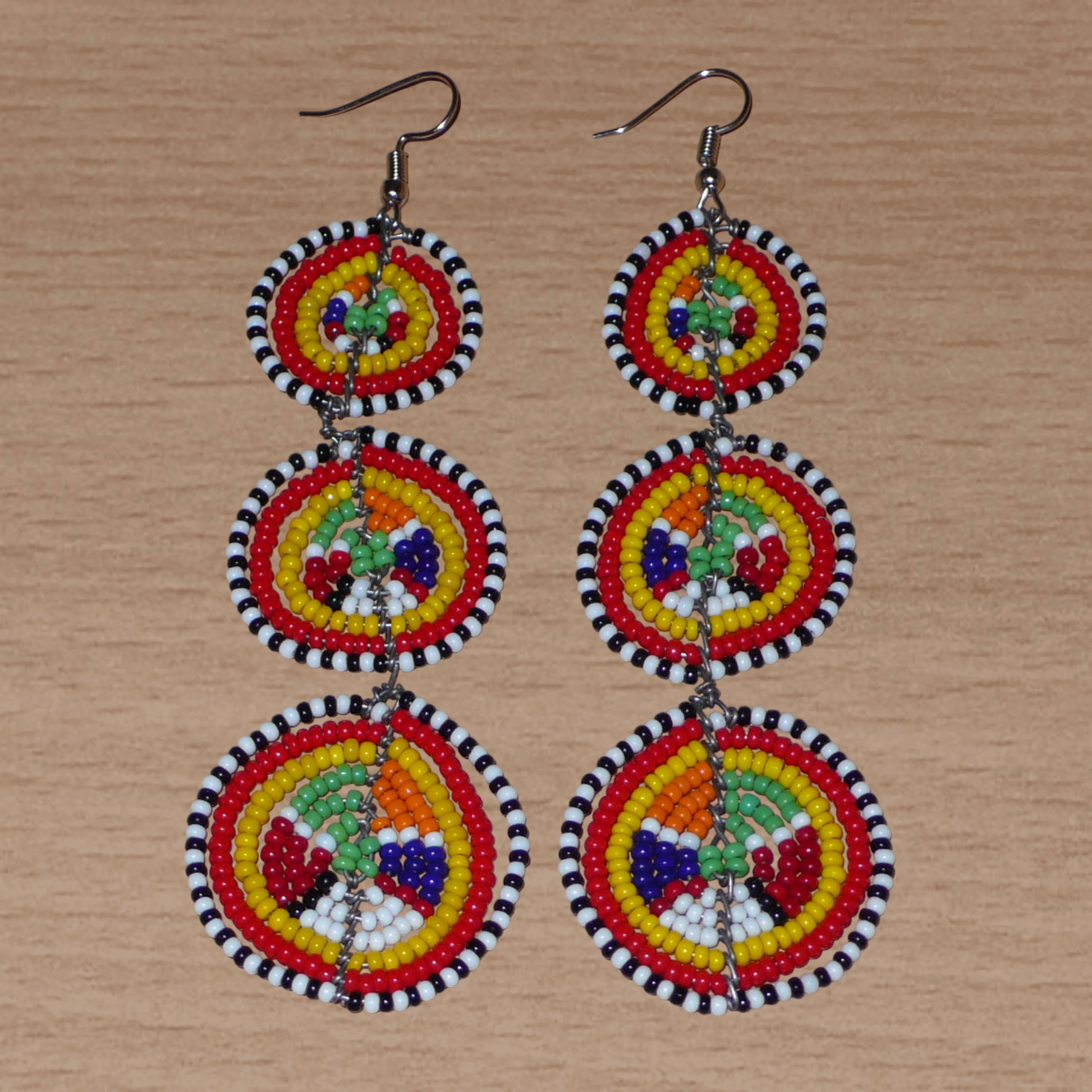 Affirmez votre style avec ces boucles d'oreilles africaines traditionnelles de confection artisanale Massai, évoquant le style afro chic des années 70. Elles se composent de perles de rocaille multicolores enfilées sur des fils de fer montés en forme de trois cercles superposés. Ces boucles d'oreilles mesurent 11 cm de long et 3.5 cm de large ; elles se portent avec des crochets en acier inoxydable sur des oreilles percées.