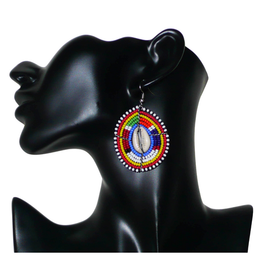 Boucles d'oreilles africaines traditionnelles, aux couleurs et motifs ethniques Massai, de fabrication artisanale kenyane. Elles se composent de perles de rocaille bleues et multicolores et de coquillages cauris fixés sur des fils de fer montés en forme de boucliers Massai. Ces boucles d'oreilles de taille moyenne mesurent 6.5 cm de long et 4 cm de large ; elles se portent avec des crochets en acier inoxydable sur des oreilles percées.