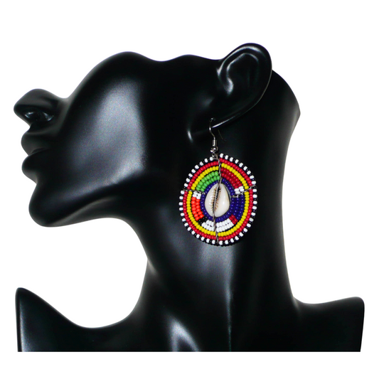 Boucles d'oreilles africaines traditionnelles aux motifs ethniques caractéristiques de l'artisanat Massai. De fabrication kenyane, elles se composent de perles de rocaille bleu foncé et multicolores et de cauris fixés sur des fils de fer montés en forme de boucliers Massai. Ces boucles d'oreilles de taille moyenne mesurent 6 cm de long et 4 cm de large ; elles se portent avec des crochets en acier inoxydable sur des oreilles percées.