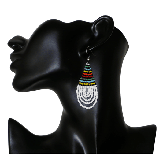 Boucles d'oreilles africaines à motifs traditionnels zoulous en forme de gouttes composées d'un tissage de perles de rocaille blanches et multicolores. Elles mesurent 7 cm de long et 2,5 cm de large et se portent sur des oreilles percées.