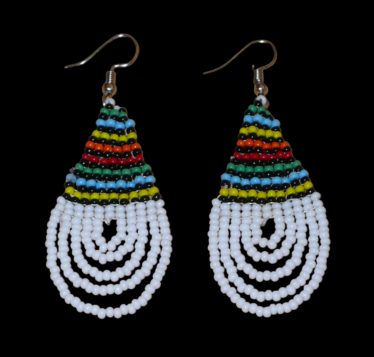 Boucles d'oreilles africaines à motifs traditionnels zoulous en forme de gouttes composées d'un tissage de perles de rocaille blanches et multicolores. Elles mesurent 7 cm de long et 2,5 cm de large et se portent sur des oreilles percées.