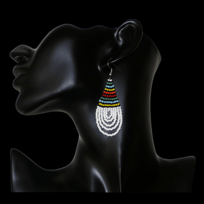 Boucles d'oreilles africaines à motifs traditionnels zoulous en forme de gouttes composées d'un tissage de perles de rocaille blanches et multicolores. Elles mesurent 7 cm de long et 2,5 cm de large et se portent sur des oreilles percées.