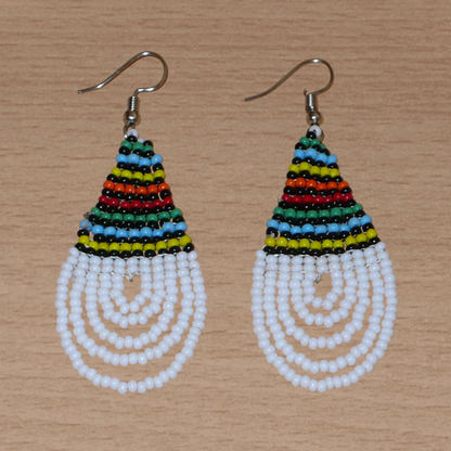 Boucles d'oreilles africaines à motifs traditionnels zoulous en forme de gouttes composées d'un tissage de perles de rocaille blanches et multicolores. Elles mesurent 7 cm de long et 2,5 cm de large et se portent sur des oreilles percées.