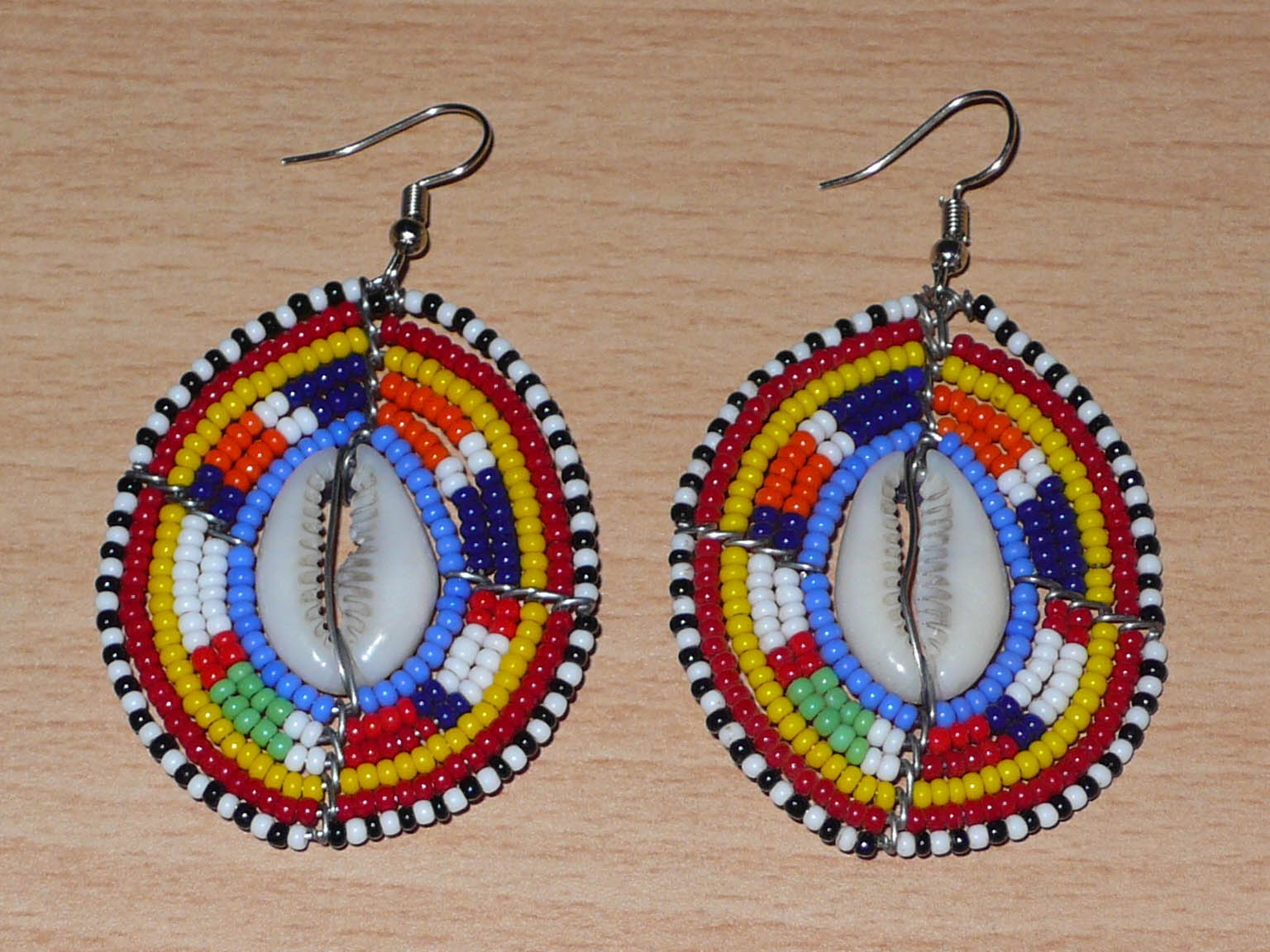 Boucles d'oreilles africaines en forme de boucliers Massai composées de perles de rocaille multicolores et de coquillages cauris. Elles mesurent 7 cm de long et 4 cm de large. Timeless Fineries