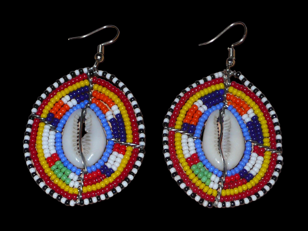 Boucles d'oreilles africaines en forme de boucliers Massai composées de perles de rocaille multicolores et de coquillages cauris. Elles mesurent 7 cm de long et 4 cm de large.