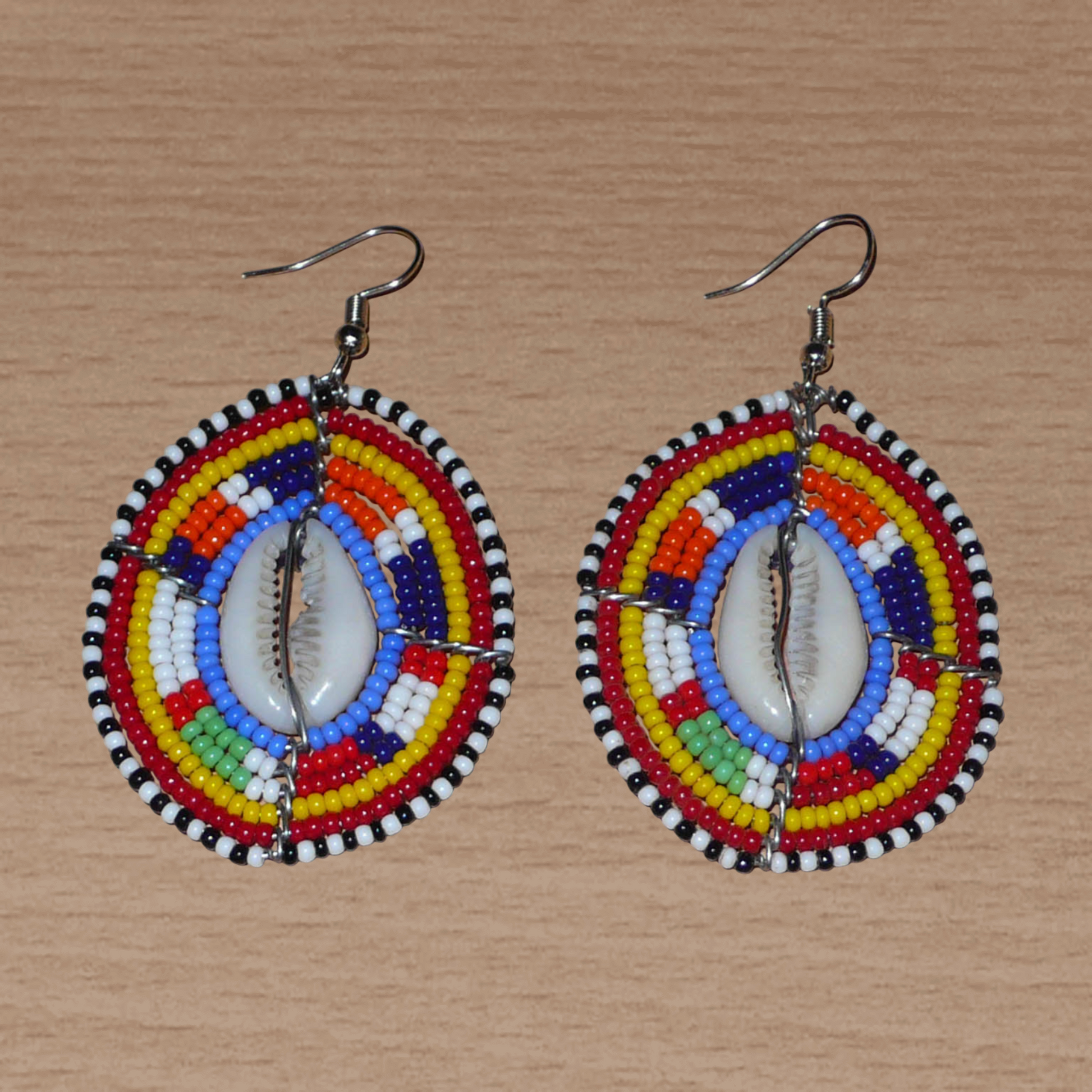 Boucles d'oreilles africaines en forme de boucliers Massai composées de perles de rocaille multicolores et de coquillages cauris. Elles mesurent 7 cm de long et 4 cm de large.