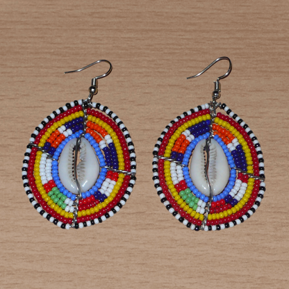Boucles d'oreilles africaines en forme de boucliers Massai composées de perles de rocaille multicolores et de coquillages cauris. Elles mesurent 7 cm de long et 4 cm de large.