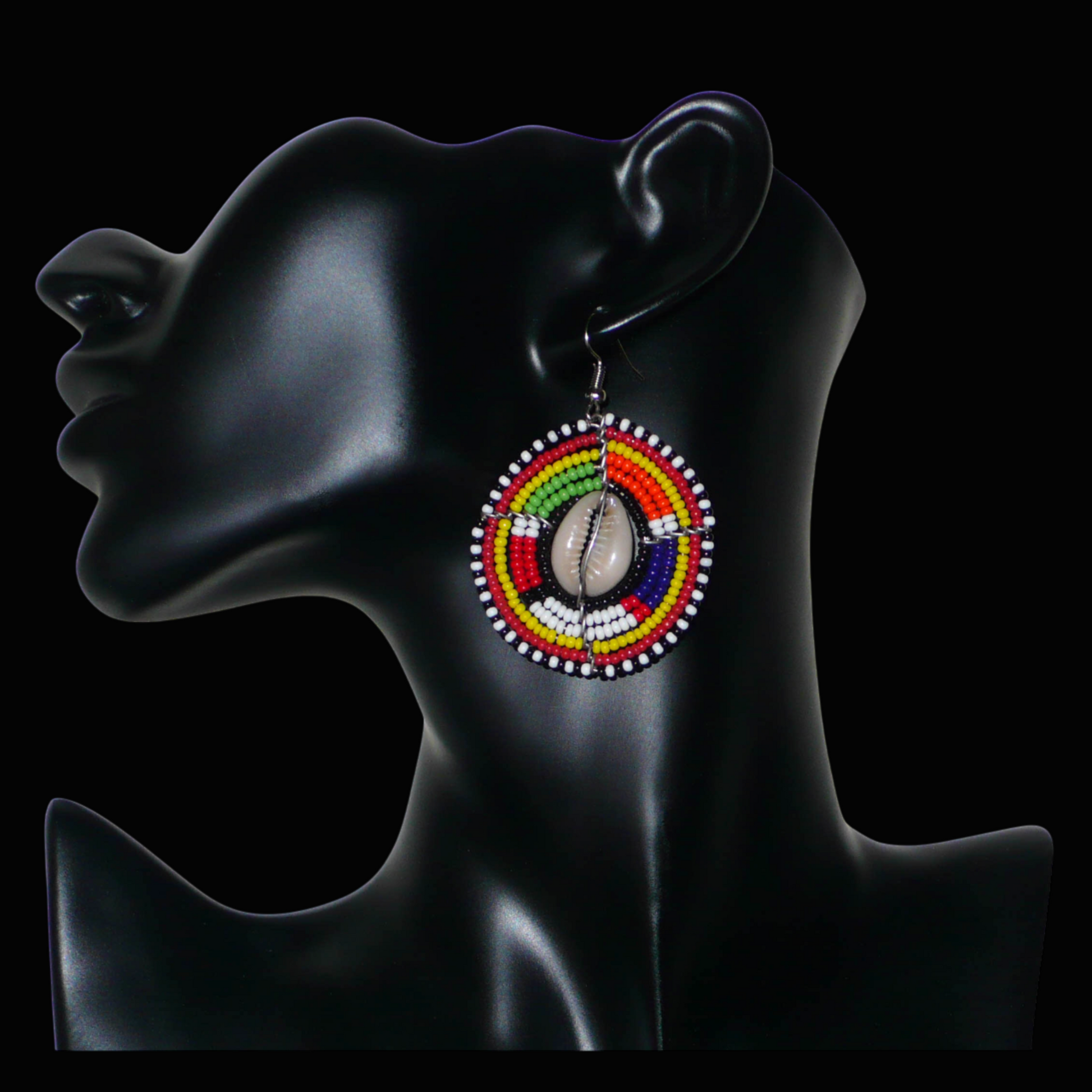 Boucles d'oreilles africaines Massai à motifs ethniques traditionnels : de fabrication artisanale kenyane, elles se composent de perles de rocaille noires et multicolores et de coquillages cauris fixés sur des fils de fer montés en forme de boucliers Massai. De taille moyenne, ces boucles d'oreilles aux accents exotiques mesurent 6.5 cm de long et 4 cm de large ; elles se portent avec des crochets en acier inoxydable sur des oreilles percées.