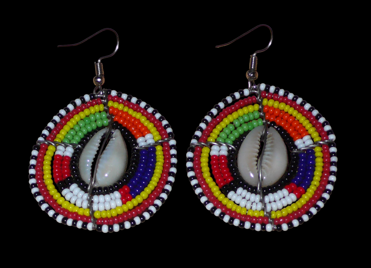 Boucles d'oreilles africaines Massai à motifs ethniques traditionnels : de fabrication artisanale kenyane, elles se composent de perles de rocaille noires et multicolores et de coquillages cauris fixés sur des fils de fer montés en forme de boucliers Massai. De taille moyenne, ces boucles d'oreilles aux accents exotiques mesurent 6.5 cm de long et 4 cm de large ; elles se portent avec des crochets en acier inoxydable sur des oreilles percées.