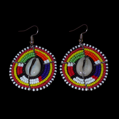 Boucles d'oreilles africaines Massai à motifs ethniques traditionnels : de fabrication artisanale kenyane, elles se composent de perles de rocaille noires et multicolores et de coquillages cauris fixés sur des fils de fer montés en forme de boucliers Massai. De taille moyenne, ces boucles d'oreilles aux accents exotiques mesurent 6.5 cm de long et 4 cm de large ; elles se portent avec des crochets en acier inoxydable sur des oreilles percées.