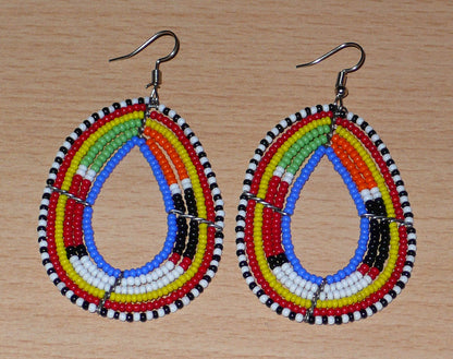 Boucles d'oreilles ethniques multi-rangs à motifs traditionnels Massai composées de perles de rocaille bleues et multicolores glissées sur six rangs de fils de fer montés en forme de gouttes. Elles mesurent 7.5 cm de long et 4 cm de large, et se portent avec des crochets en acier inoxydable sur des oreilles percées.