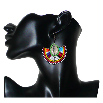 Ajoutez une touche afro chic à votre style avec cette jolie paire de boucles d'oreilles africaines issues de l'artisanat traditionnel Massai. Ces boucles d'oreilles aux accents exotiques se composent de perles de rocaille vertes et multicolores et de coquillages cauris. De taille moyenne, elles mesurent 6 cm de long et 4.5 cm de large, et se portent avec des crochets en acier inoxydable sur des oreilles percées.