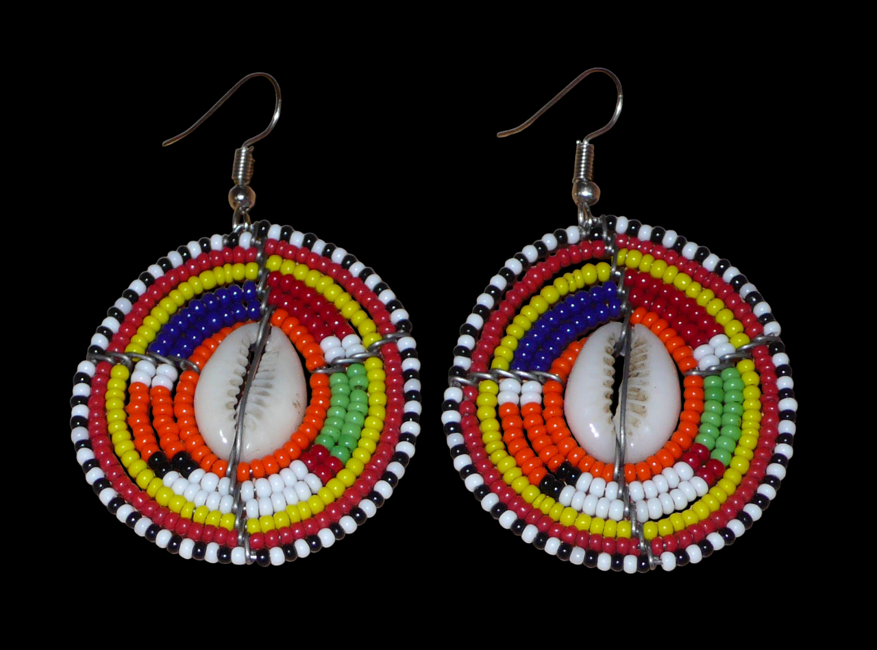 Boucles d'oreilles africaines aux couleurs exotiques et motifs ethniques caractéristiques de l'artisanat traditionnel Massai. Confectionnées au Kenya, elles se composent de perles de rocaille orange et multicolores et de coquillages fixés sur des fils de fer montés en forme de boucliers Massai. Ces boucles d'oreilles de taille moyenne mesurent 6 cm de long et 4 cm de large, et se portent avec des crochets en acier inoxydable sur des oreilles percées.