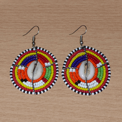 Boucles d'oreilles africaines aux couleurs exotiques et motifs ethniques caractéristiques de l'artisanat traditionnel Massai. Confectionnées au Kenya, elles se composent de perles de rocaille orange et multicolores et de coquillages fixés sur des fils de fer montés en forme de boucliers Massai. Ces boucles d'oreilles de taille moyenne mesurent 6 cm de long et 4 cm de large, et se portent avec des crochets en acier inoxydable sur des oreilles percées.