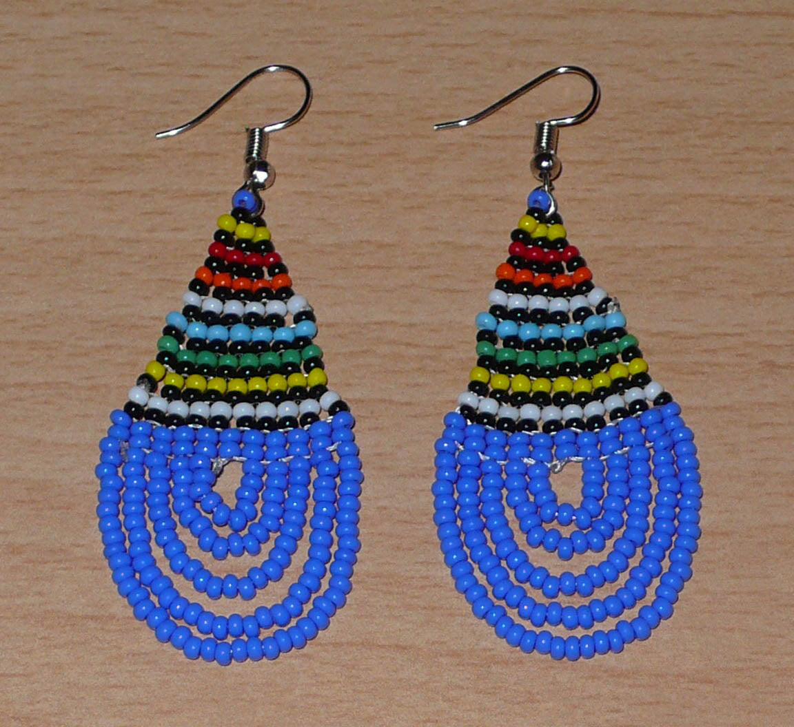 Boucles d'oreilles sud-africaines zouloues en forme de gouttes composées d'un tissage de perles de rocaille bleues et multicolores. Elles mesurent 7 cm de long et 2,5 cm de large et se portent sur des oreilles percées.