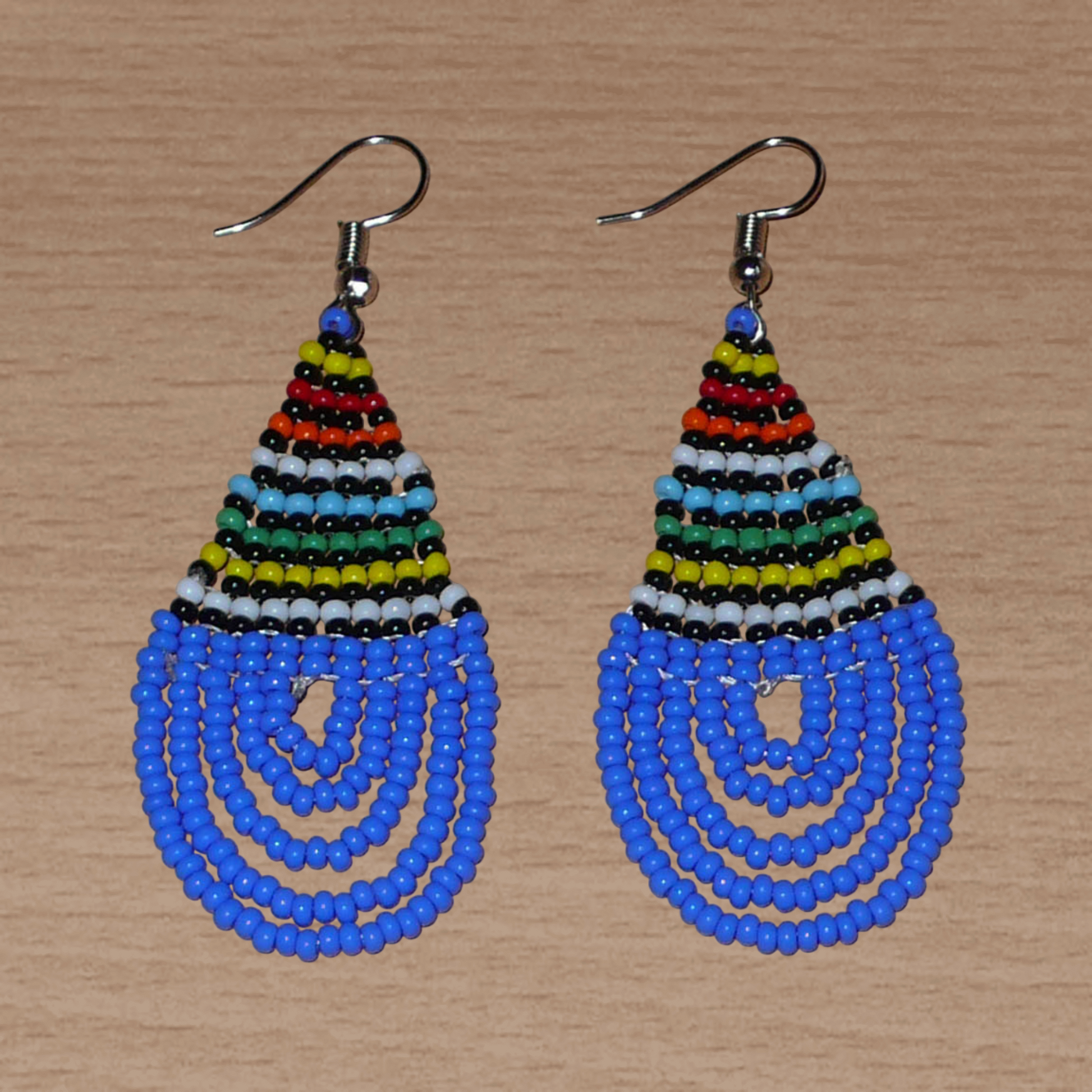 Boucles d'oreilles sud-africaines zouloues en forme de gouttes composées d'un tissage de perles de rocaille bleues et multicolores. Elles mesurent 7 cm de long et 2,5 cm de large et se portent sur des oreilles percées.