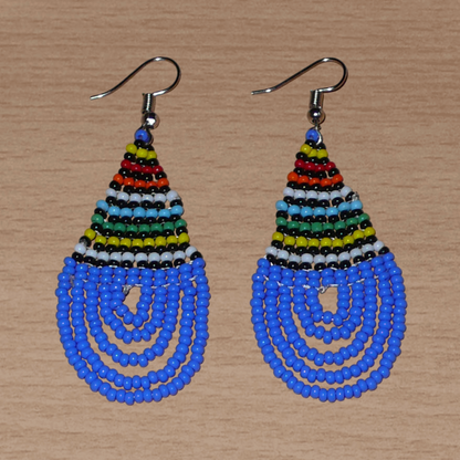 Boucles d'oreilles sud-africaines zouloues en forme de gouttes composées d'un tissage de perles de rocaille bleues et multicolores. Elles mesurent 7 cm de long et 2,5 cm de large et se portent sur des oreilles percées.
