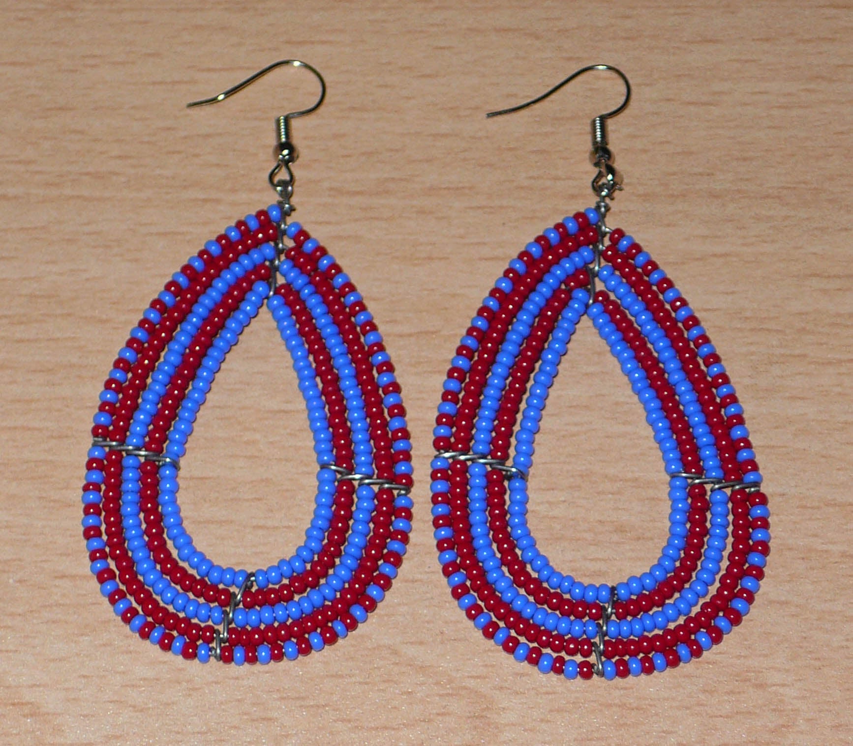 Boucles d'oreilles kenyanes bicolores rouges et bleues en forme de gouttes faites de perles de rocailles. Elles mesurent 8,5 cm de long et 4 cm de large et se portent sur des oreilles percées.