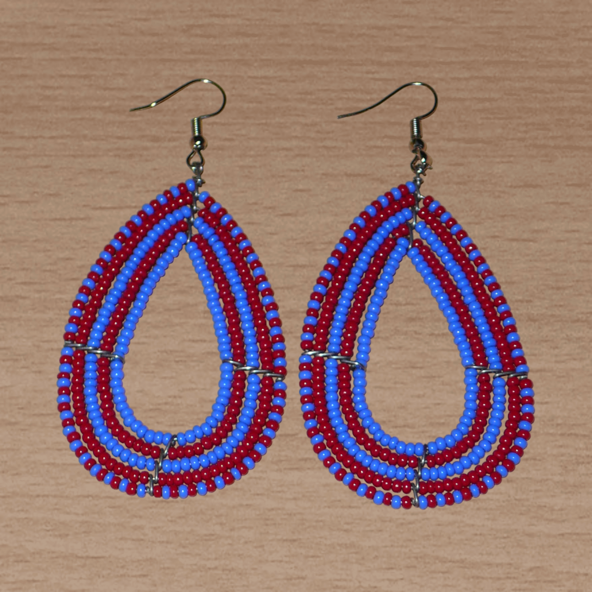 Boucles d'oreilles kenyanes bicolores rouges et bleues en forme de gouttes faites de perles de rocailles. Elles mesurent 8,5 cm de long et 4 cm de large et se portent sur des oreilles percées.