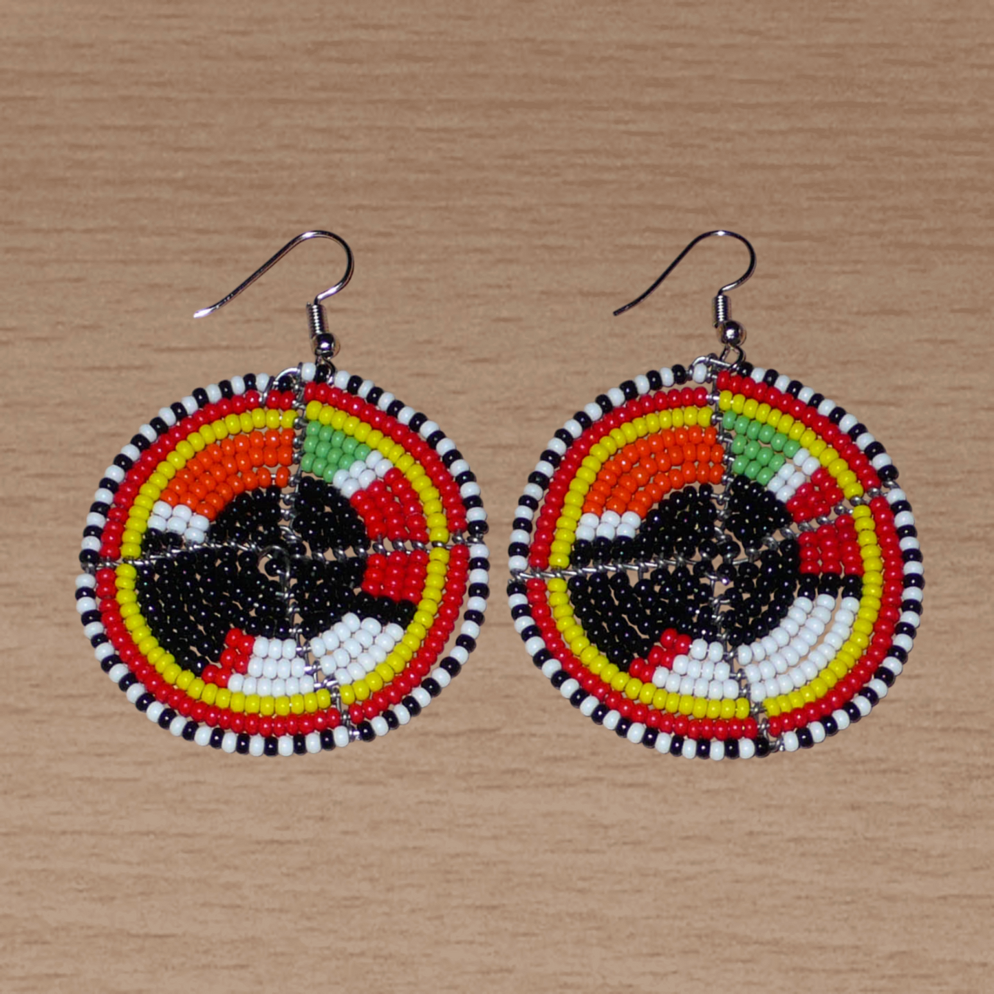 Boucles d'oreilles ethniques rondes composées de perles de rocaille noires et multicolores. De taille moyenne, ces boucles d'oreilles africaines de tradition Massai mesurent 6,5 cm de long et 4,5 cm de large ; elles se portent avec des crochets en acier inoxydable sur des oreilles percées.