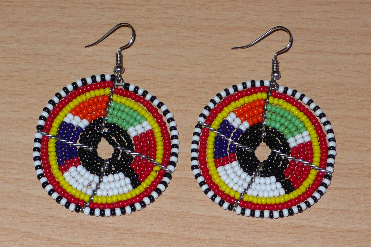 Boucles d'oreilles ethniques Massai composées de perles de rocaille multicolores glissées sur des fils de fer montés en forme de cercles. Elles mesurent 6,5 cm de long et 4,5 cm de large et se portent avec des crochets en acier inoxydable sur des oreilles percées.