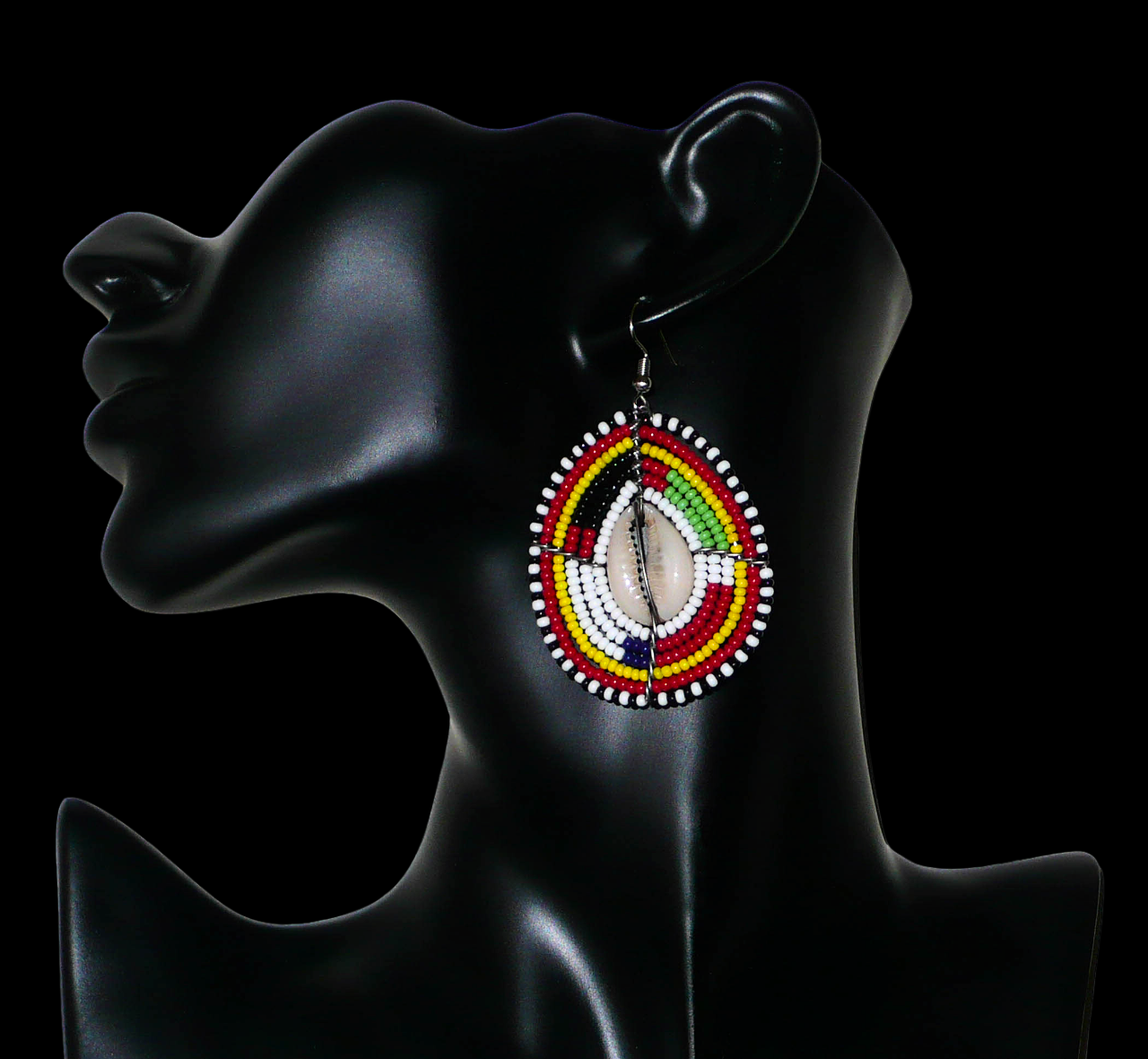 Boucles d'oreilles africaines aux couleurs et motifs ethniques Massai. Elles se composent de perles de rocaille multicolores enfilées sur des fils de fer montés en forme de boucliers Massai ; des coquillages sont incrustés en leur centre. Elles mesurent 7 cm de long et 4 cm de large et se portent avec des crochets en acier inoxydable sur des oreilles percées. Timeless Fineries
