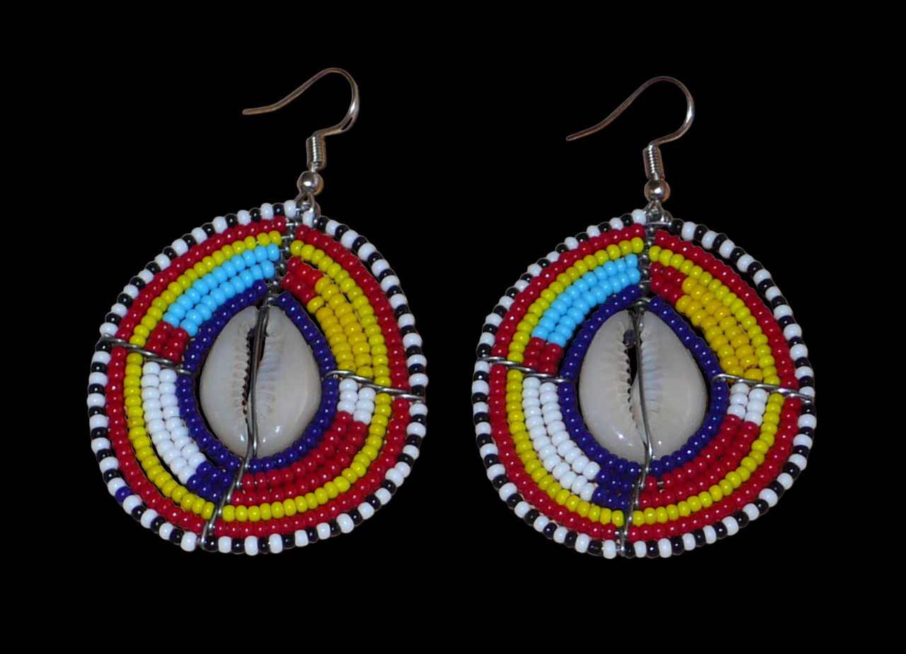 Boucles d'oreilles africaines traditionnelles aux couleurs et motifs ethniques Massai. Elles se composent de perles de rocaille multicolores enfilées sur des fils de fer montés en forme de boucliers Massai ; des coquillages sont incrustés en leur centre. Elles mesurent 7 cm de long et 4 cm de large et se portent avec des crochets en acier inoxydable sur des oreilles percées.