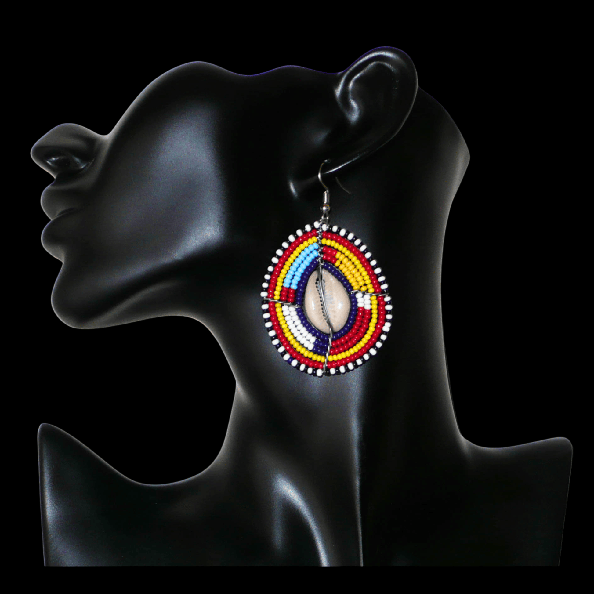 Boucles d'oreilles africaines traditionnelles aux couleurs et motifs ethniques Massai. Elles se composent de perles de rocaille multicolores enfilées sur des fils de fer montés en forme de boucliers Massai ; des coquillages sont incrustés en leur centre. Elles mesurent 7 cm de long et 4 cm de large et se portent avec des crochets en acier inoxydable sur des oreilles percées.