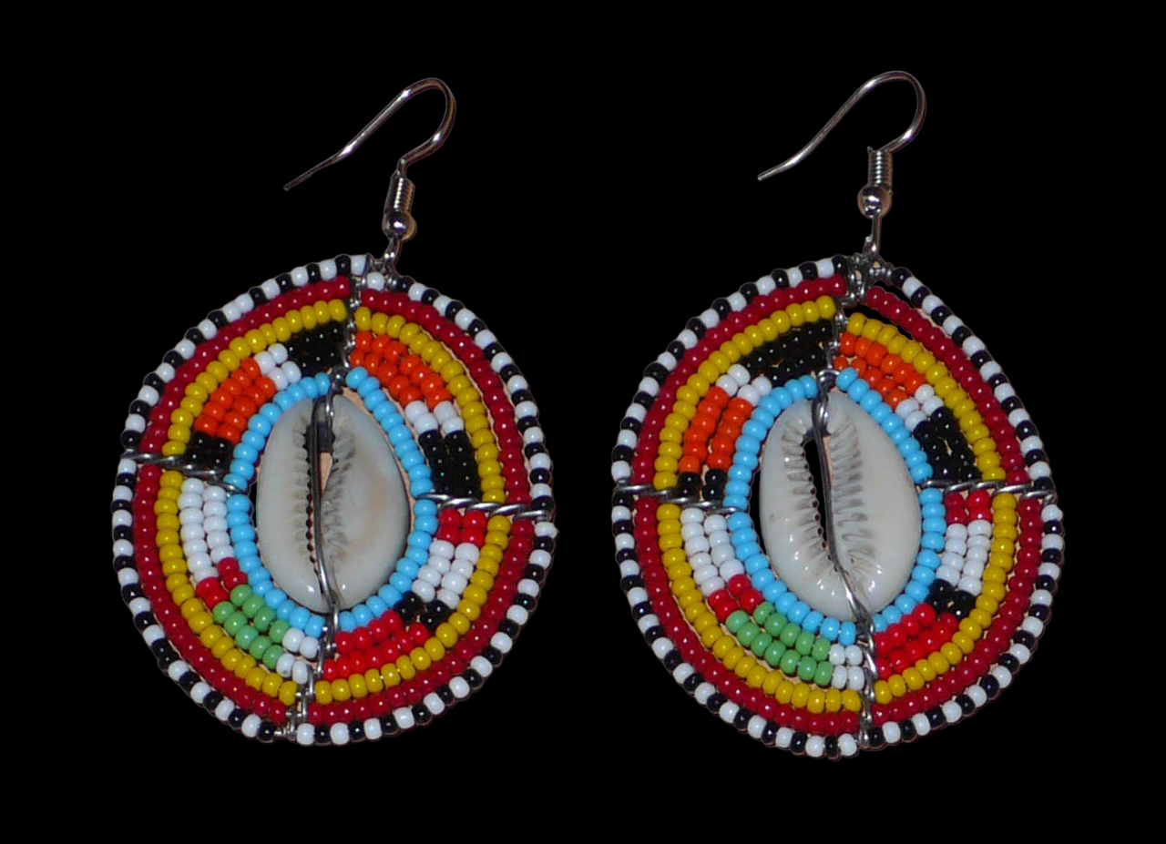Boucles d'oreilles africaines ethniques en perles de rocaille colorées et coquillages cauris montés en forme de boucliers Massai. Elles mesurent 7 cm de long et 4.5 cm de large, et se portent avec des crochets en acier inoxydable sur des oreilles percées. 