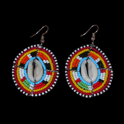Boucles d'oreilles africaines ethniques en perles de rocaille colorées et coquillages cauris montés en forme de boucliers Massai. Elles mesurent 7 cm de long et 4.5 cm de large, et se portent avec des crochets en acier inoxydable sur des oreilles percées. 