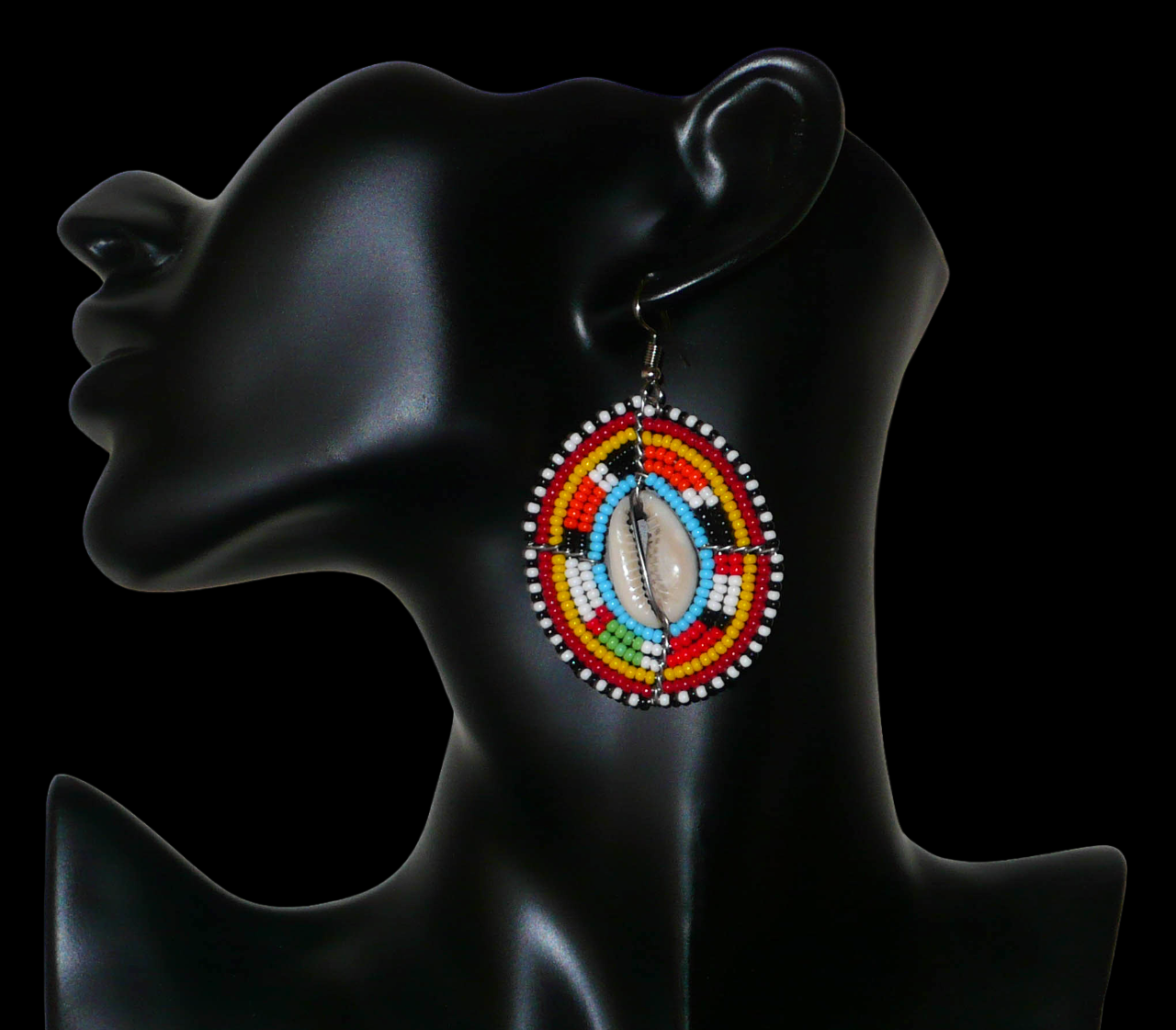 Boucles d'oreilles africaines ethniques en perles de rocaille colorées et coquillages cauris montés en forme de boucliers Massai. Elles mesurent 7 cm de long et 4.5 cm de large, et se portent avec des crochets en acier inoxydable sur des oreilles percées. 