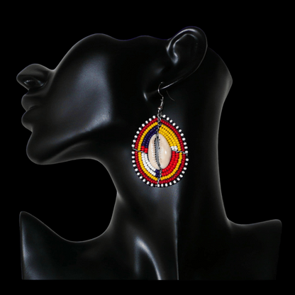 Boucles d'oreilles africaines ethniques en forme de boucliers Massai composées de perles et de coquillages cauris. De taille moyenne, elles mesurent 6,5 cm de long et 3,5 cm de large.