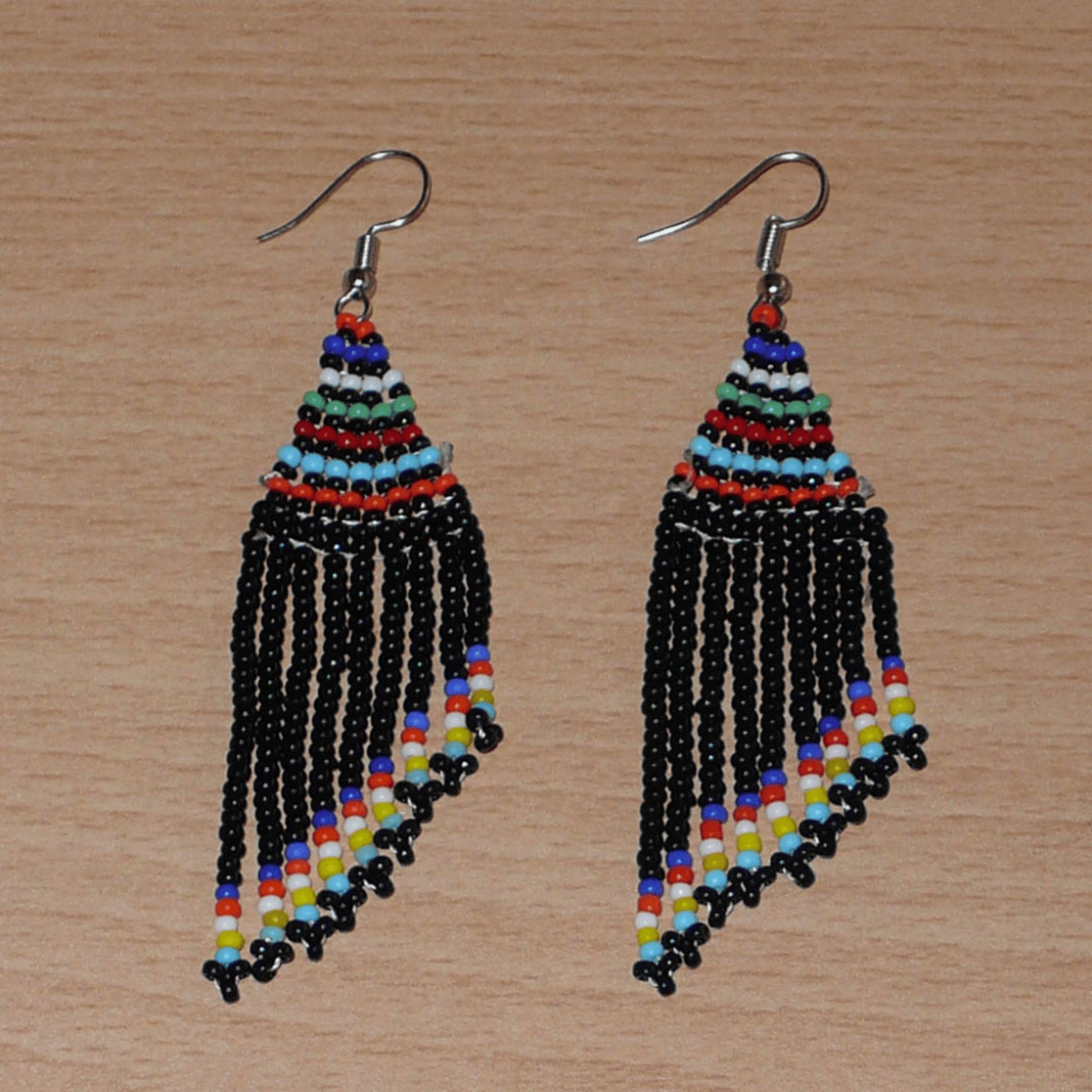 Boucles d'oreilles ethniques de tradition sud-africaine à franges perlées composées de perles de rocaille noires et multicolores. Elles mesurent 8,5 cm de long et 2 cm de large et se portent avec des crochets en acier inoxydable sur des oreilles percées.