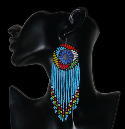 Longues boucles d'oreilles sud-africaines traditionnelles à franges et motifs zoulous composées de perles de rocaille bleu ciel et multicolores. Elles mesurent 14,5 cm de long et 4,5 cm de large, et se portent avec des crochets en acier inoxydable sur des oreilles percées.