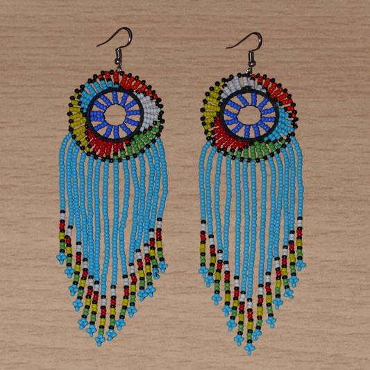Longues boucles d'oreilles sud-africaines traditionnelles à franges et motifs zoulous composées de perles de rocaille bleu ciel et multicolores. Elles mesurent 14,5 cm de long et 4,5 cm de large, et se portent avec des crochets en acier inoxydable sur des oreilles percées.