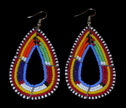 Longues boucles d'oreilles africaines Massai en forme de gouttes composées de perles de rocaille bleues et multicolores. Elles mesurent 8,5 cm de long et 4 cm de large et se portent avec des crochets en acier inoxydable sur des oreilles percées. Timeless Fineries
