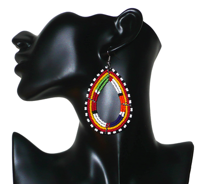 Longues boucles d'oreilles africaines à motifs et couleurs ethniques. Fabriquées par des femmes de la tribu Massai, elles se composent de perles de rocaille multicolores enfilées sur cinq rangées de fils de fer montés en forme de gouttes. Elles mesurent 8,5 cm de long et 4,5 cm de large et se portent avec des crochets en acier inoxydable sur des oreilles percées.