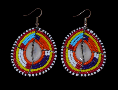Boucles d'oreilles africaines Massai composées de perles de rocaille multicolores et de coquillages cauris. Elles mesurent 7 cm de long et 4 cm de large et se portent avec des crochets en acier inoxydable sur des oreilles percées.