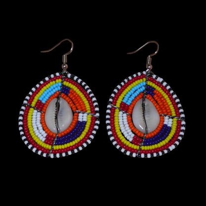 Boucles d'oreilles africaines Massai composées de perles de rocaille multicolores et de coquillages cauris. Elles mesurent 7 cm de long et 4 cm de large et se portent avec des crochets en acier inoxydable sur des oreilles percées.