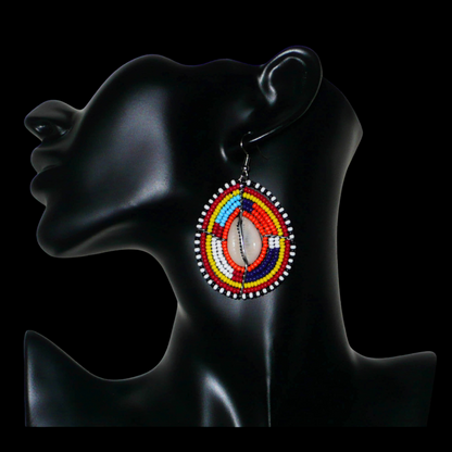 Boucles d'oreilles africaines Massai composées de perles de rocaille multicolores et de coquillages cauris. Elles mesurent 7 cm de long et 4 cm de large et se portent avec des crochets en acier inoxydable sur des oreilles percées.