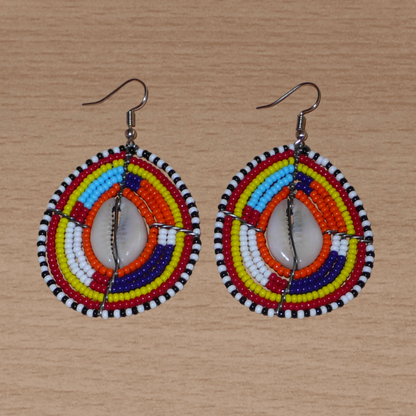 Boucles d'oreilles africaines Massai composées de perles de rocaille multicolores et de coquillages cauris. Elles mesurent 7 cm de long et 4 cm de large et se portent avec des crochets en acier inoxydable sur des oreilles percées.