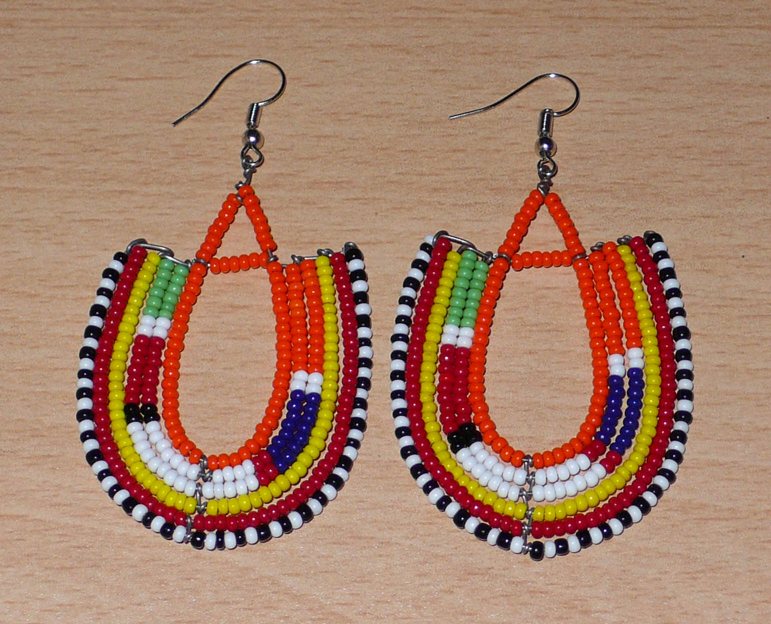 Boucles d'oreilles africaines de tradition ethnique Massai en perles de rocaille orange et multicolores montées en forme d'ancres. Elles mesurent 8 cm de long et se portent sur des oreilles percées.
