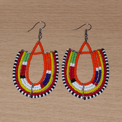 Boucles d'oreilles africaines de tradition ethnique Massai en perles de rocaille orange et multicolores montées en forme d'ancres. Elles mesurent 8 cm de long et se portent sur des oreilles percées.