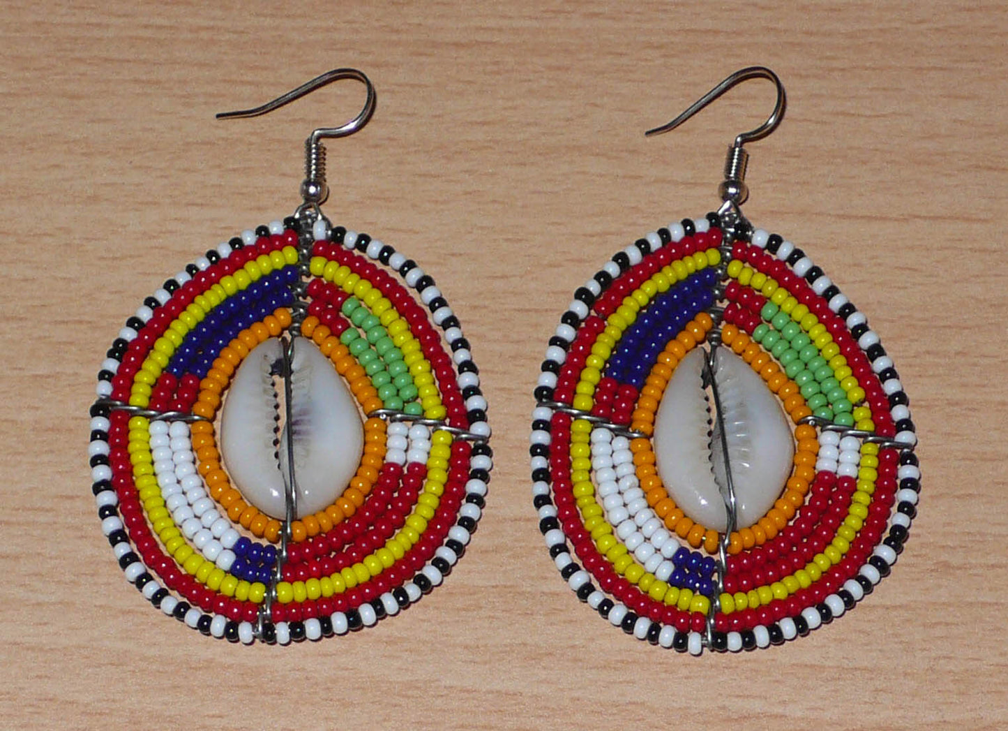 Boucles d'oreilles africaines à motifs ethniques traditionnels Massai composées de perles multicolores et de coquillages cauris ; elles mesurent 7 cm de long et 4 cm de large et se portent avec des crochets en acier inoxydable sur des oreilles percées.