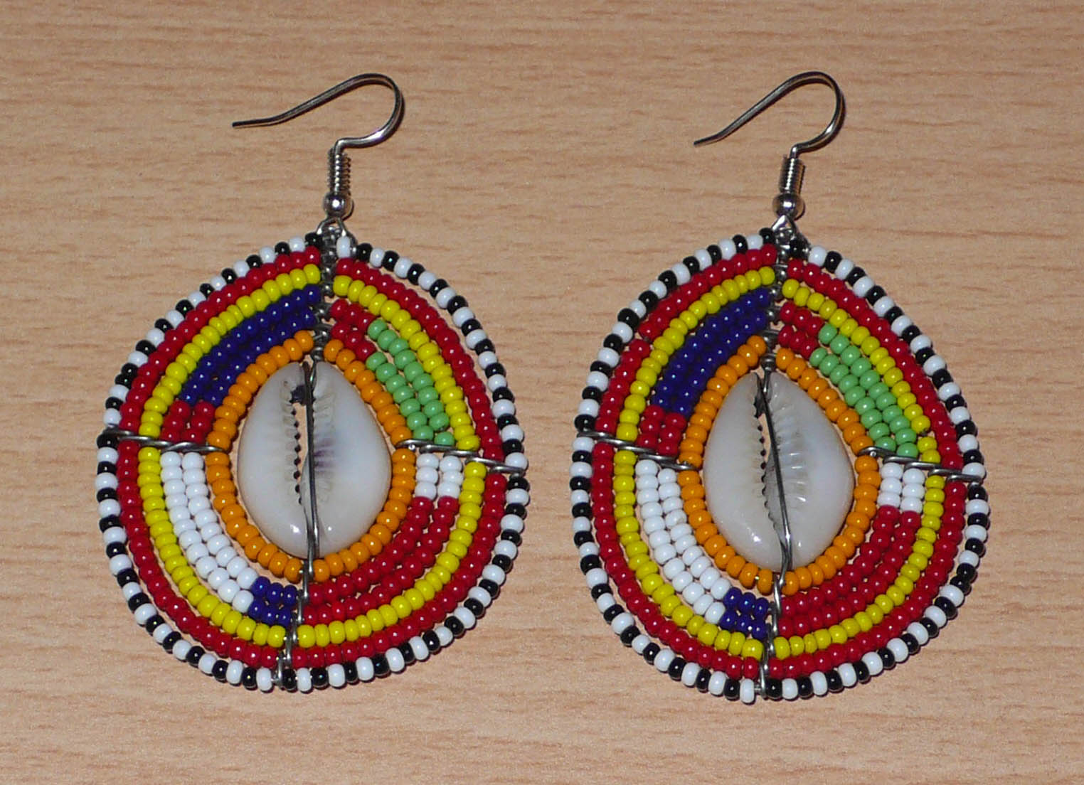 Boucles d'oreilles africaines à motifs ethniques traditionnels Massai composées de perles multicolores et de coquillages cauris ; elles mesurent 7 cm de long et 4 cm de large et se portent avec des crochets en acier inoxydable sur des oreilles percées.