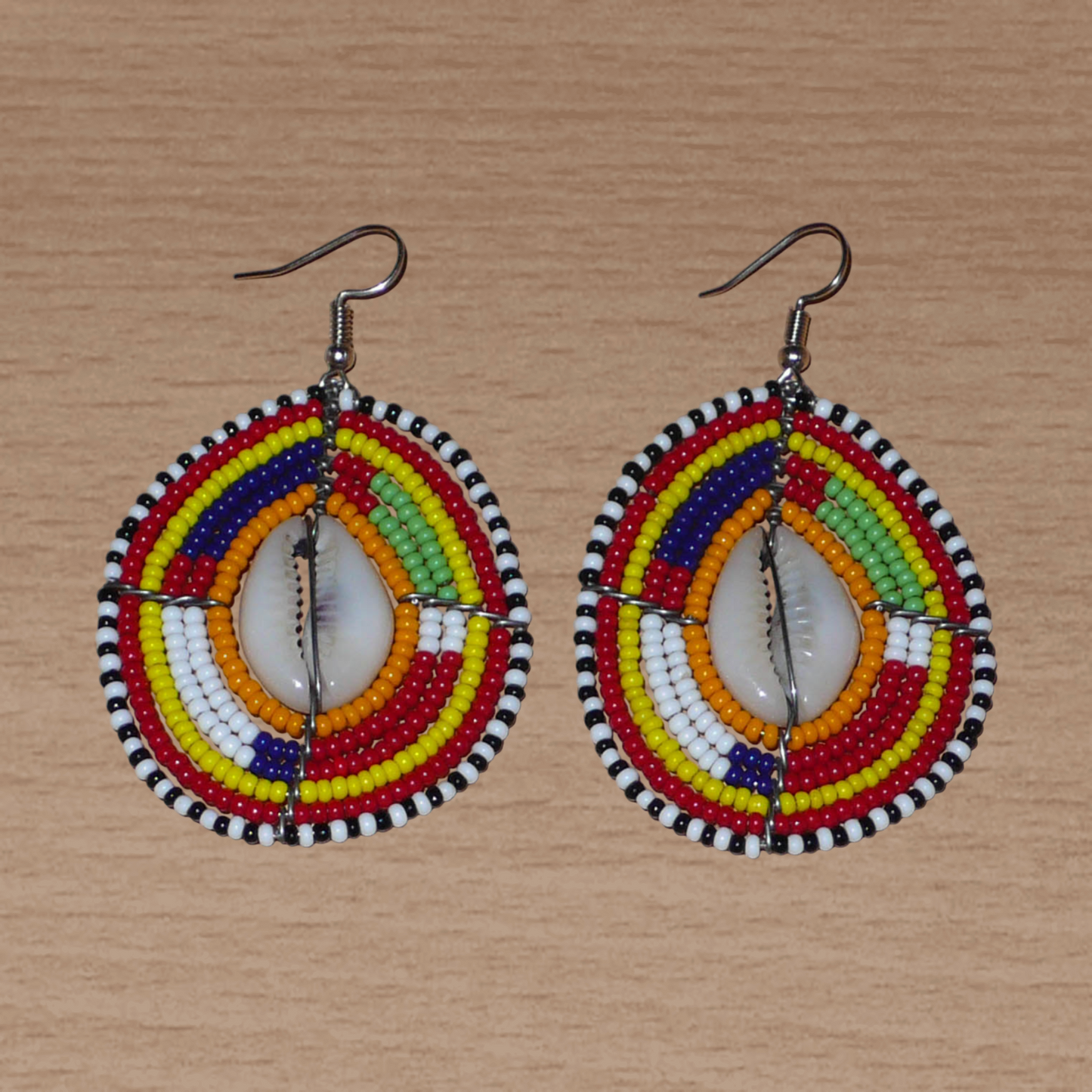 Boucles d'oreilles africaines à motifs ethniques traditionnels Massai composées de perles multicolores et de coquillages cauris ; elles mesurent 7 cm de long et 4 cm de large et se portent avec des crochets en acier inoxydable sur des oreilles percées.