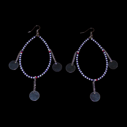 Longues boucles d'oreilles africaines  Massai composées de perles bleu foncé, blanches et rouges enfilées sur un brin de fil de fer monté en forme de goutte, et décorées de chaînettes ornées de disques métalliques. Elles mesurent 11 cm de long et 4,5 cm de large et se portent avec des crochets en acier inoxydable sur des oreilles percées.