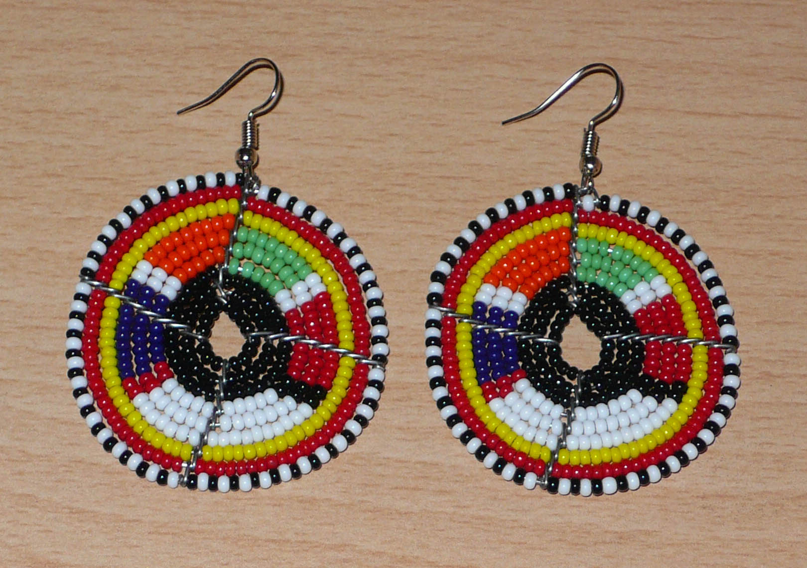 Boucles d'oreilles ethniques rondes à motifs traditionnels Massai en perles noires et multicolores. De taille moyenne, elles mesurent 6,5 cm de long et 4,5 cm de large et se portent sur des oreilles percées.