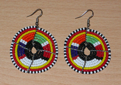Boucles d'oreilles ethniques rondes à motifs traditionnels Massai en perles noires et multicolores. De taille moyenne, elles mesurent 6,5 cm de long et 4,5 cm de large et se portent sur des oreilles percées.
