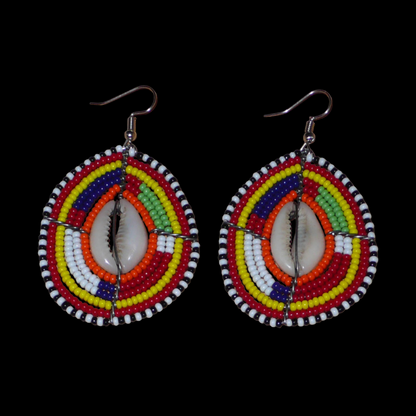Boucles d'oreilles africaines à motifs ethniques composées de perles et de coquillages montés en forme de boucliers Massai. Elles mesurent 7 cm de long et 4 cm de large et se portent sur des oreilles percées. 